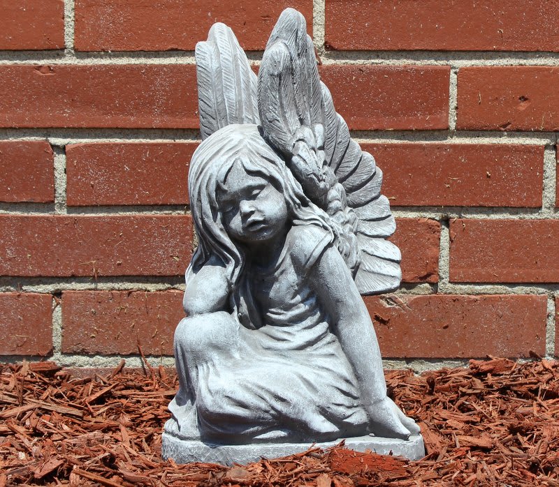 Gray angel statue of a seated child against a brick wall