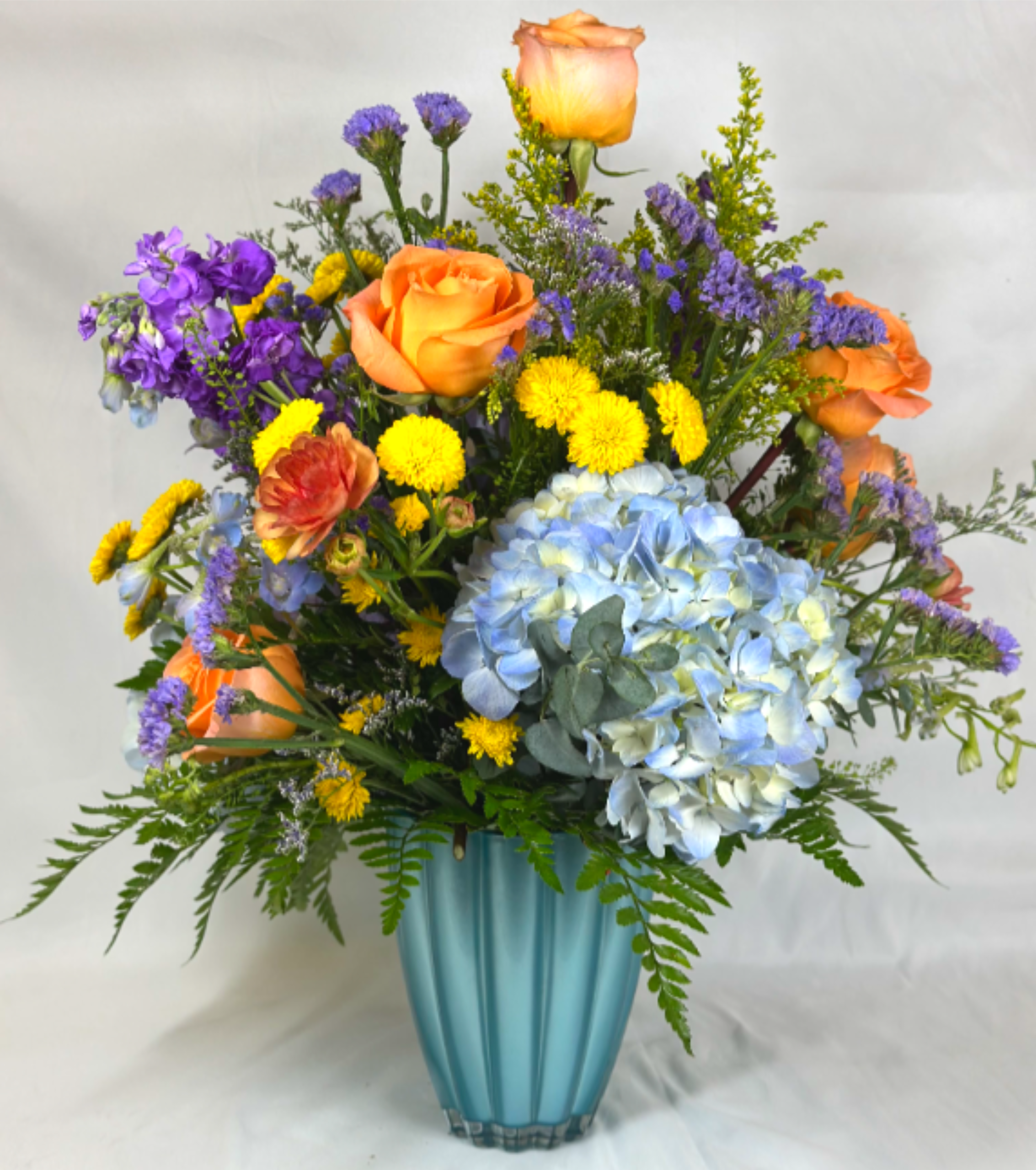 Summer By the Sea - The colors and warmth of a summer sunset along the waters edge is the inspiration behind this Leary's Flowers exclusive design. This beautiful tall arrangement features some of summer's most gorgeous flowers, like hydrangeas, roses, and ranunculus. The blue vase is a stunning turquoise and is made to last and be enjoyed for years to come. If the featured flowers are unavailable we will design your arrangement using the freshest available blooms of equal or greater value
