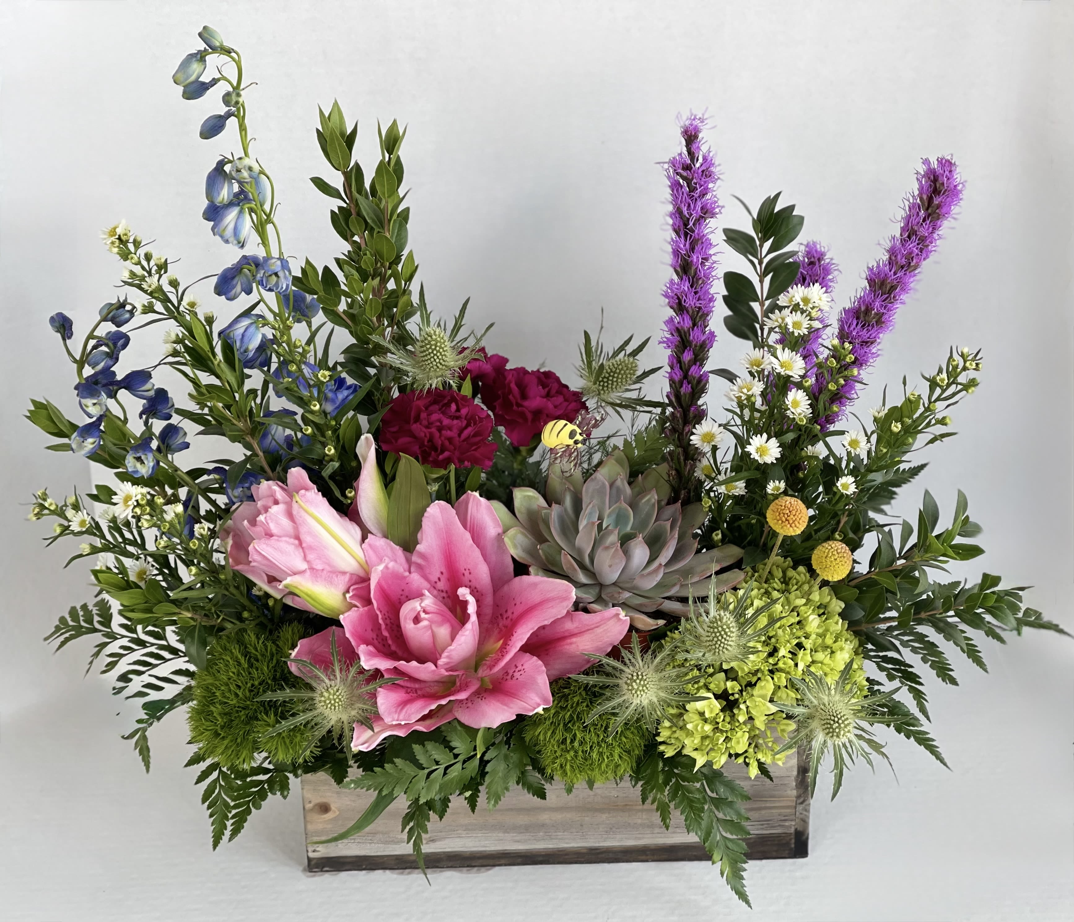 Into The Garden  - Into the Garden is a luxurious design in a wooden garden box. Incorporated in the design is blue delphinium, purple liatris, purple carnations, pink rose lily, green hydrangea, and a four inch succulent plant. Bring the garden into your home, or send a garden to a loved one to show how much you care! 