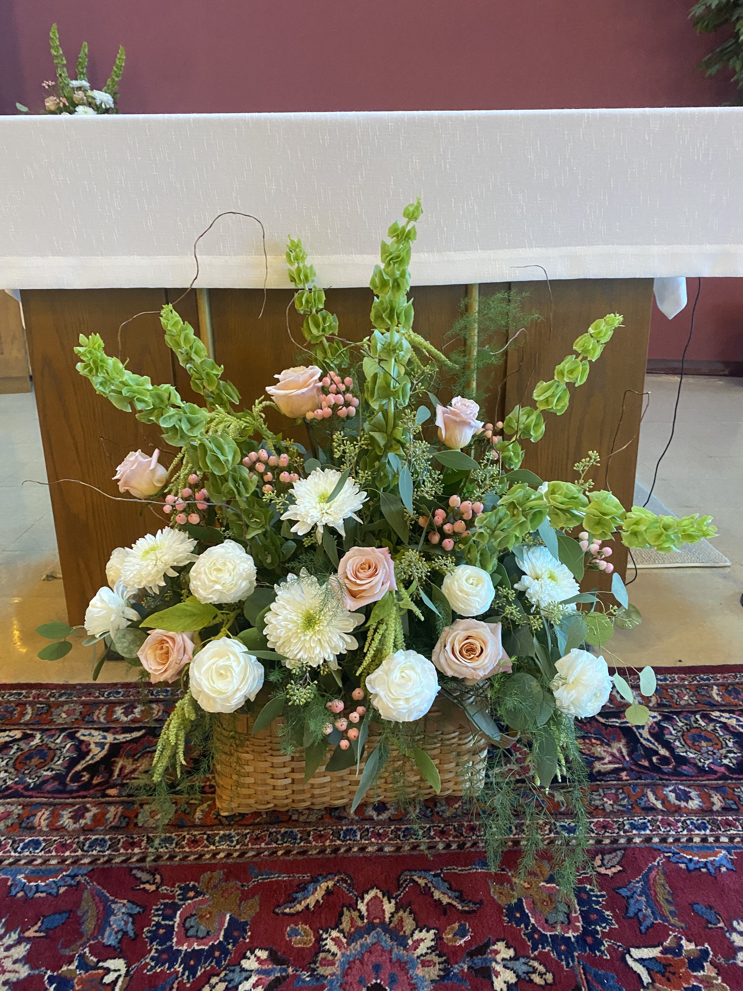Large floral arrangement with pale roses, white blooms, and green spikes in a woven basket