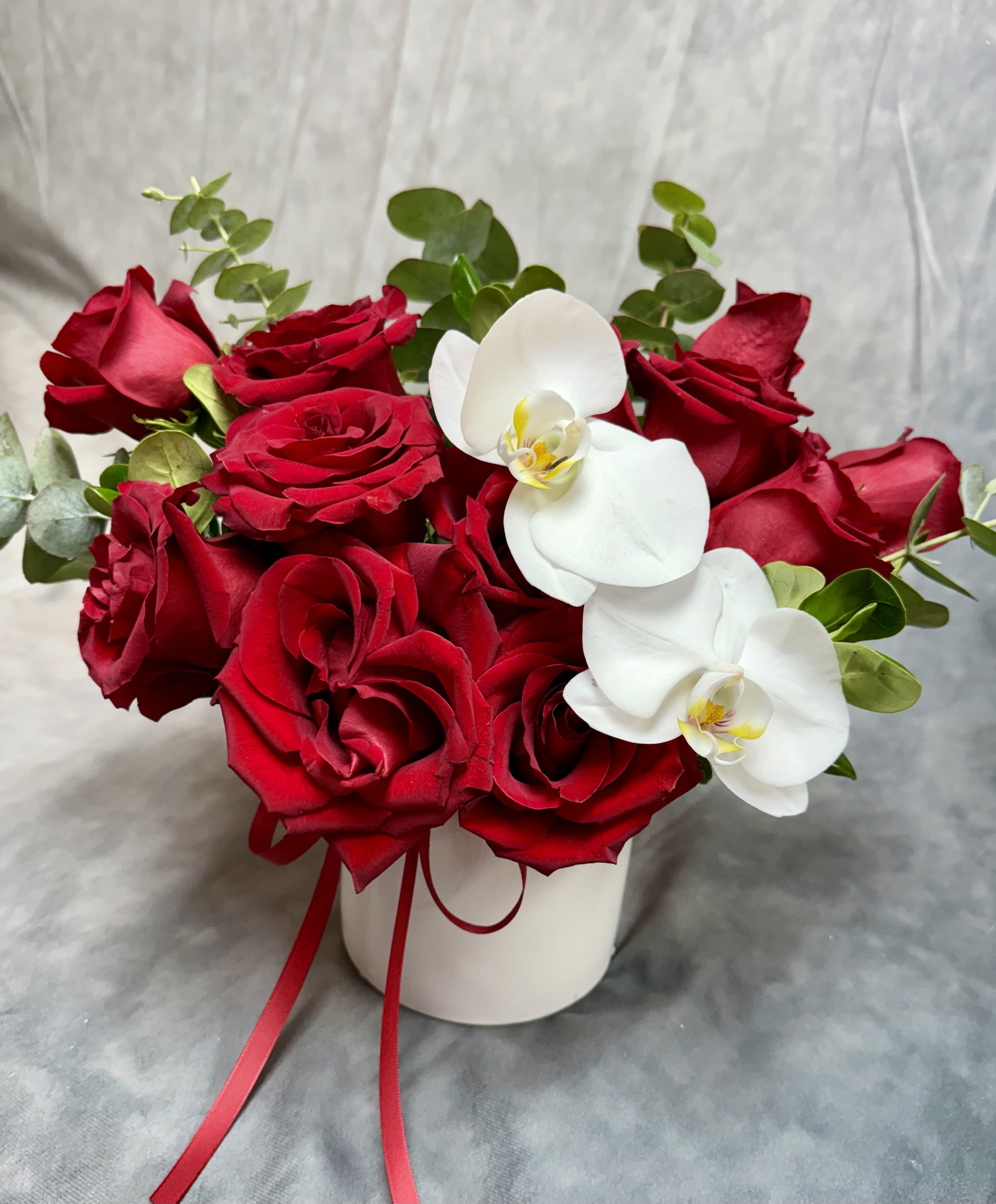 Red roses and white orchids arranged in a white vase