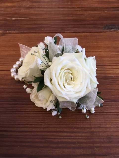 Wrist corsage of white roses and small white blooms on a pearl bracelet