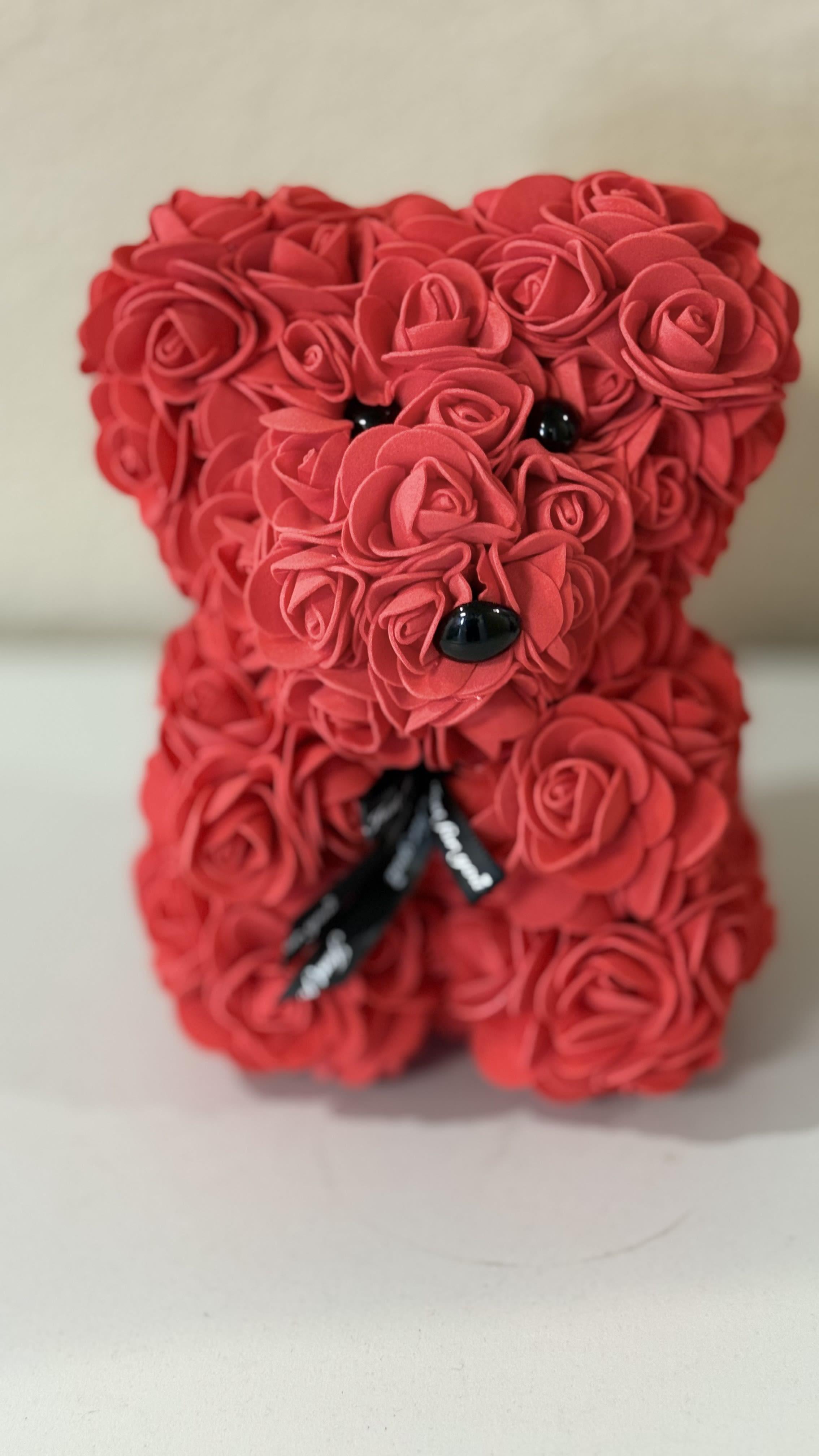 Red rose-covered teddy bear figurine with black eyes, nose, and ribbon