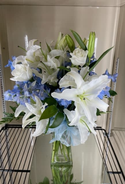 White lilies and blue flowers arranged in a clear glass vase.