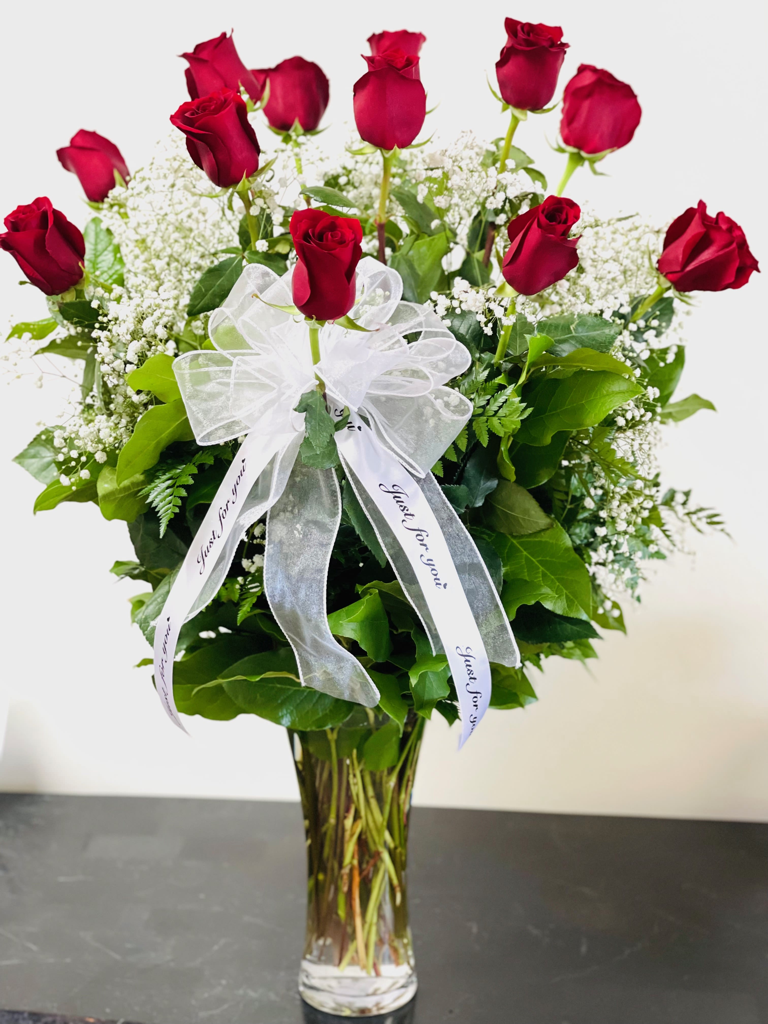Red roses in a clear glass vase with a white ribbon bow