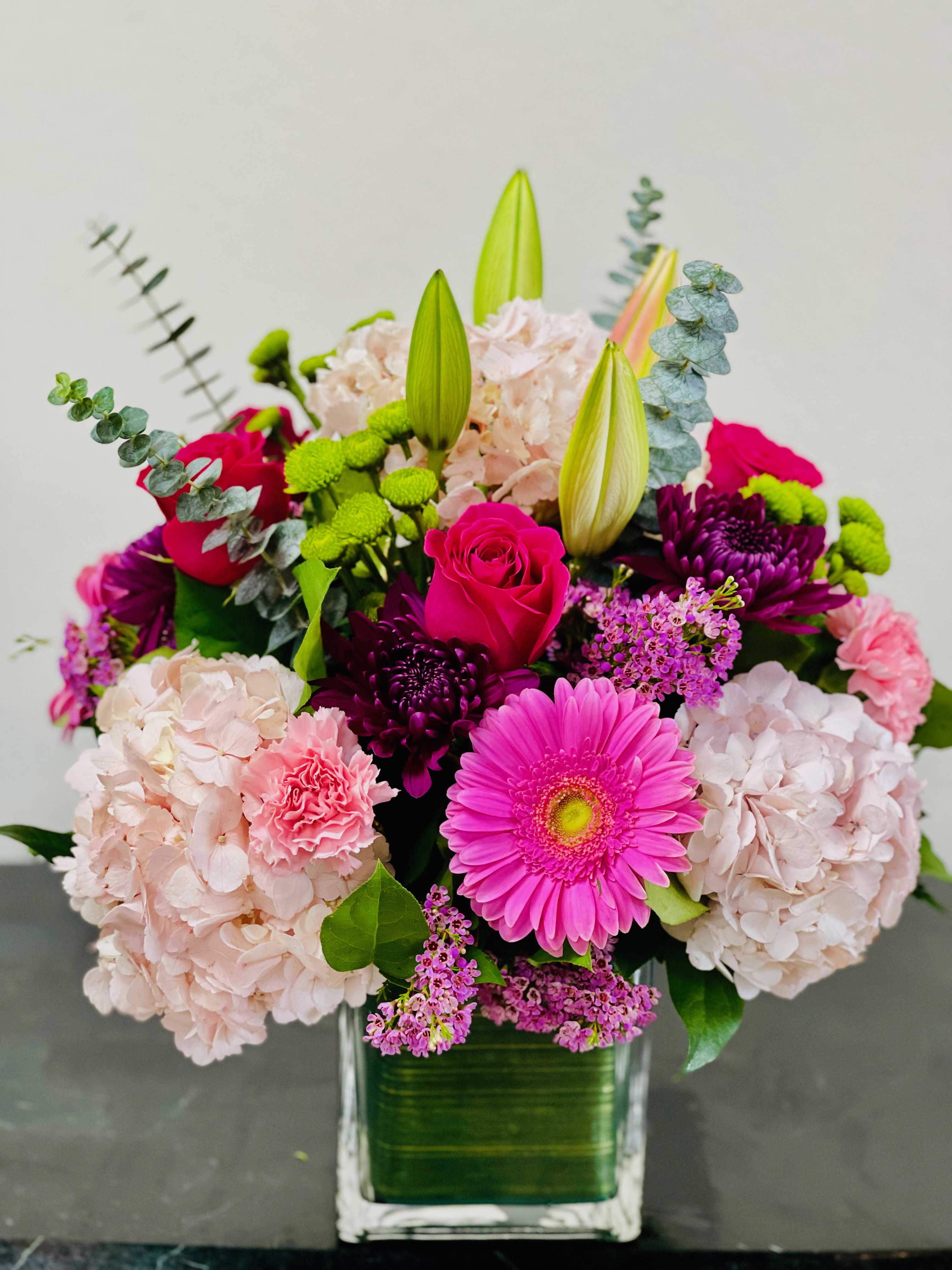 Mixed pink and purple flowers in a square glass vase