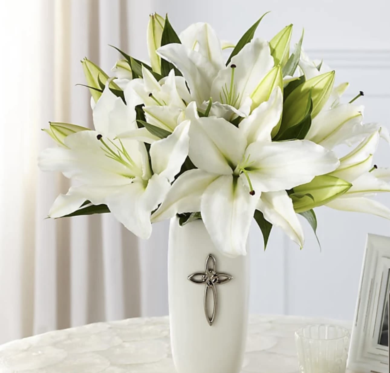 White lilies arranged in a tall white vase with a cross emblem