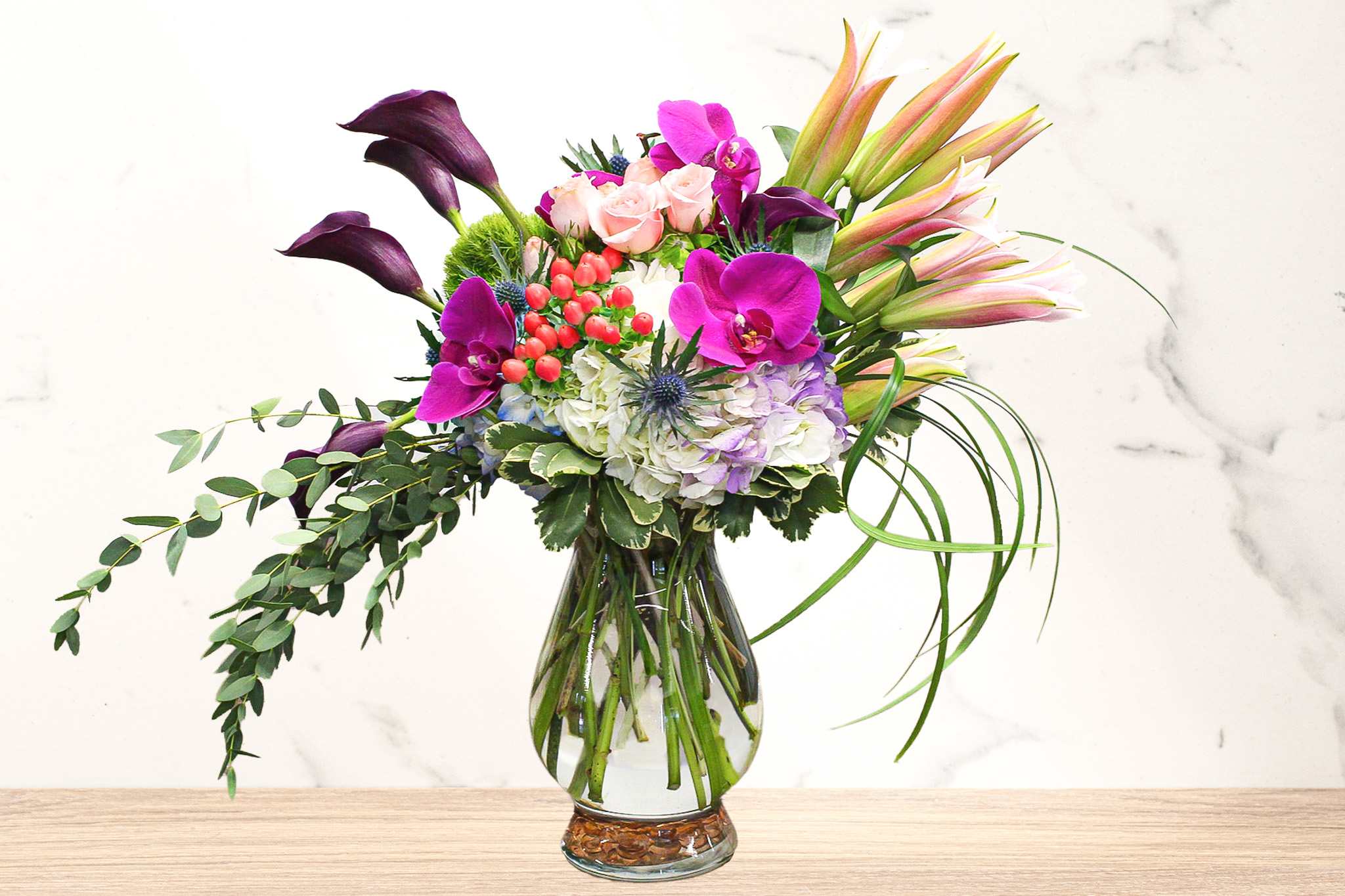 Mixed bouquet with purple orchids, pink roses, lilies, and hydrangea in a glass vase