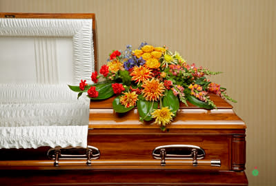Colorful floral spray on a wooden casket beside a white interior lining