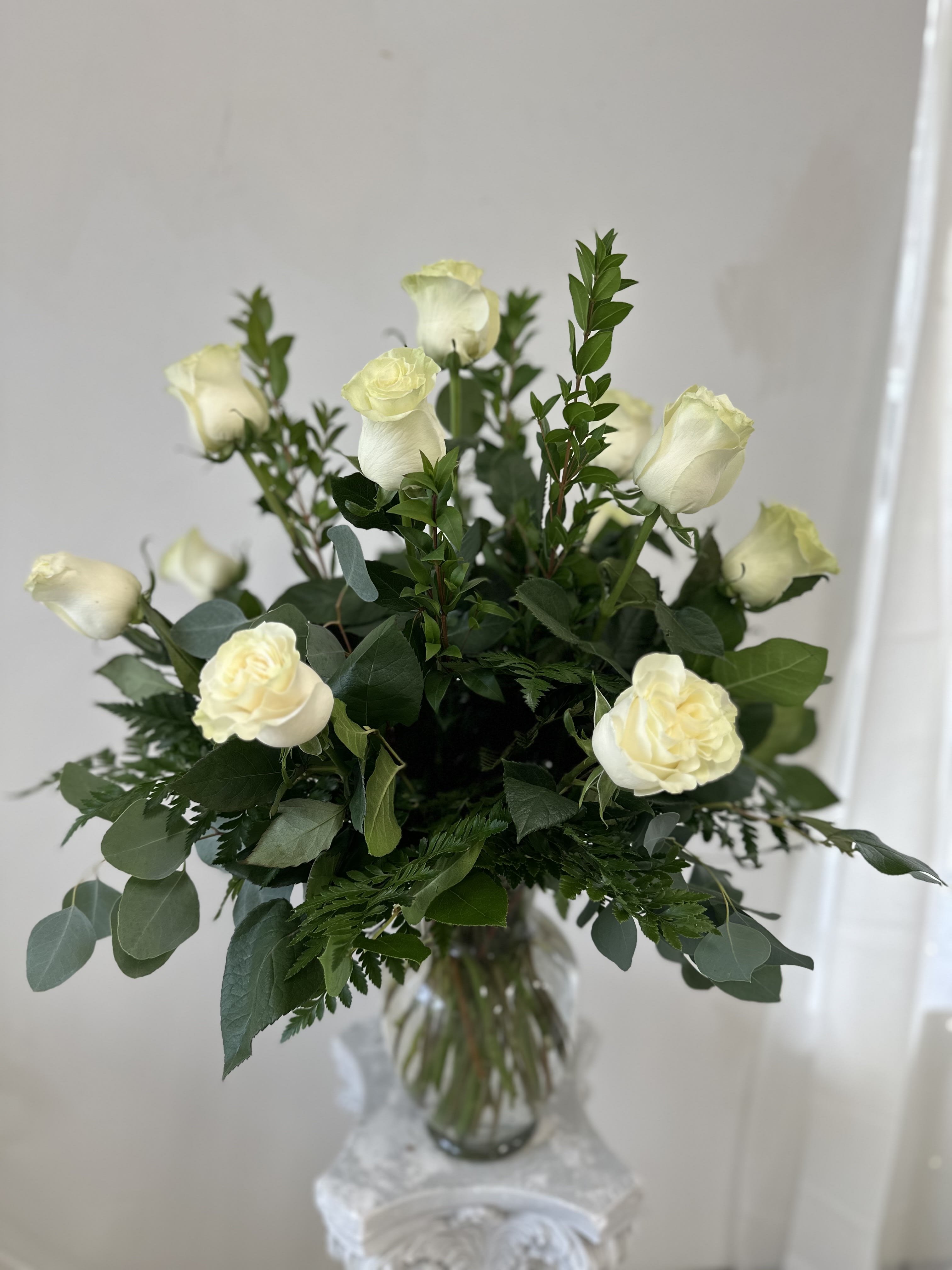White roses arranged in a clear glass vase with mixed greenery