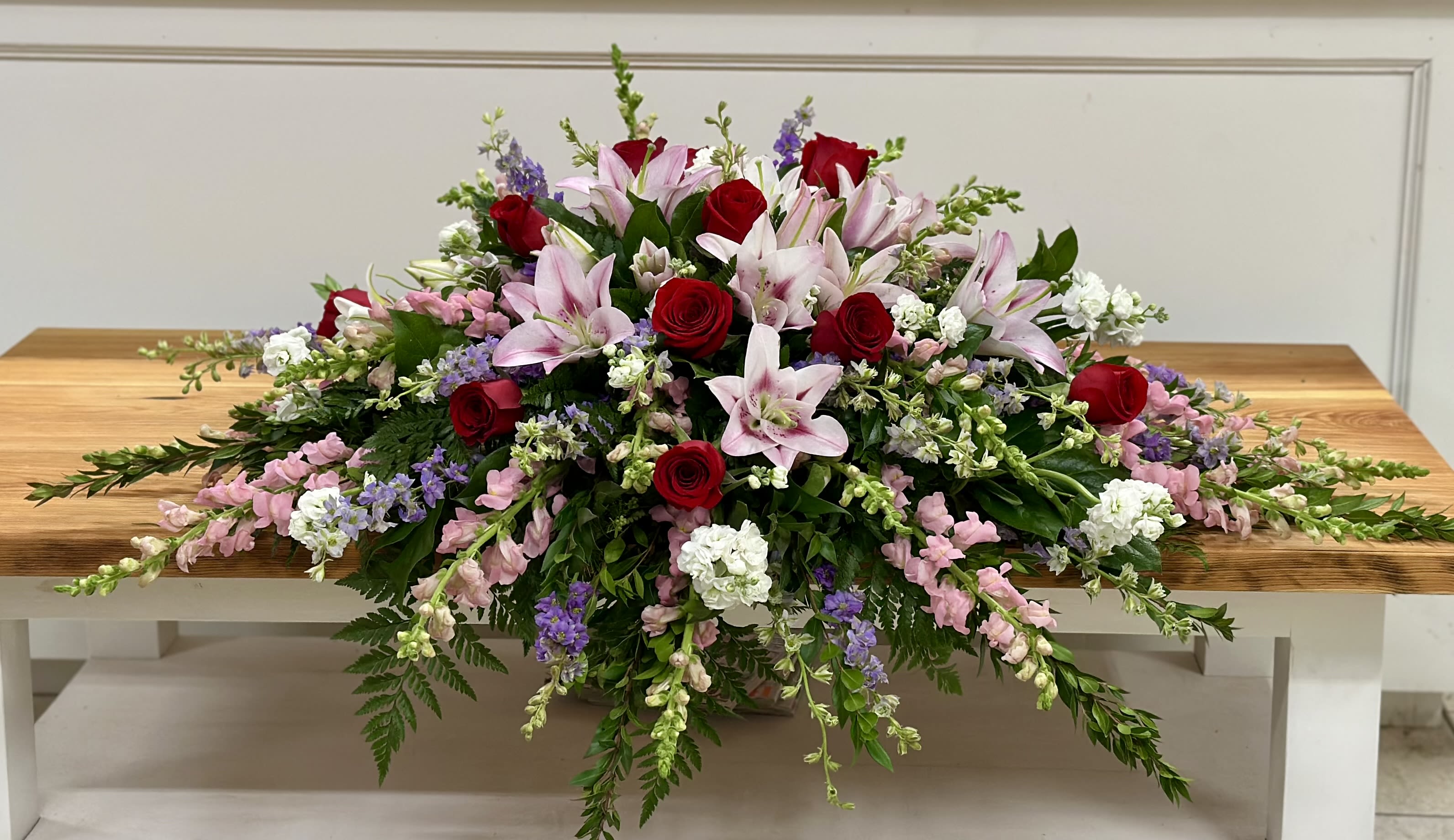 Long floral arrangement with red roses and pink lilies on a wooden table