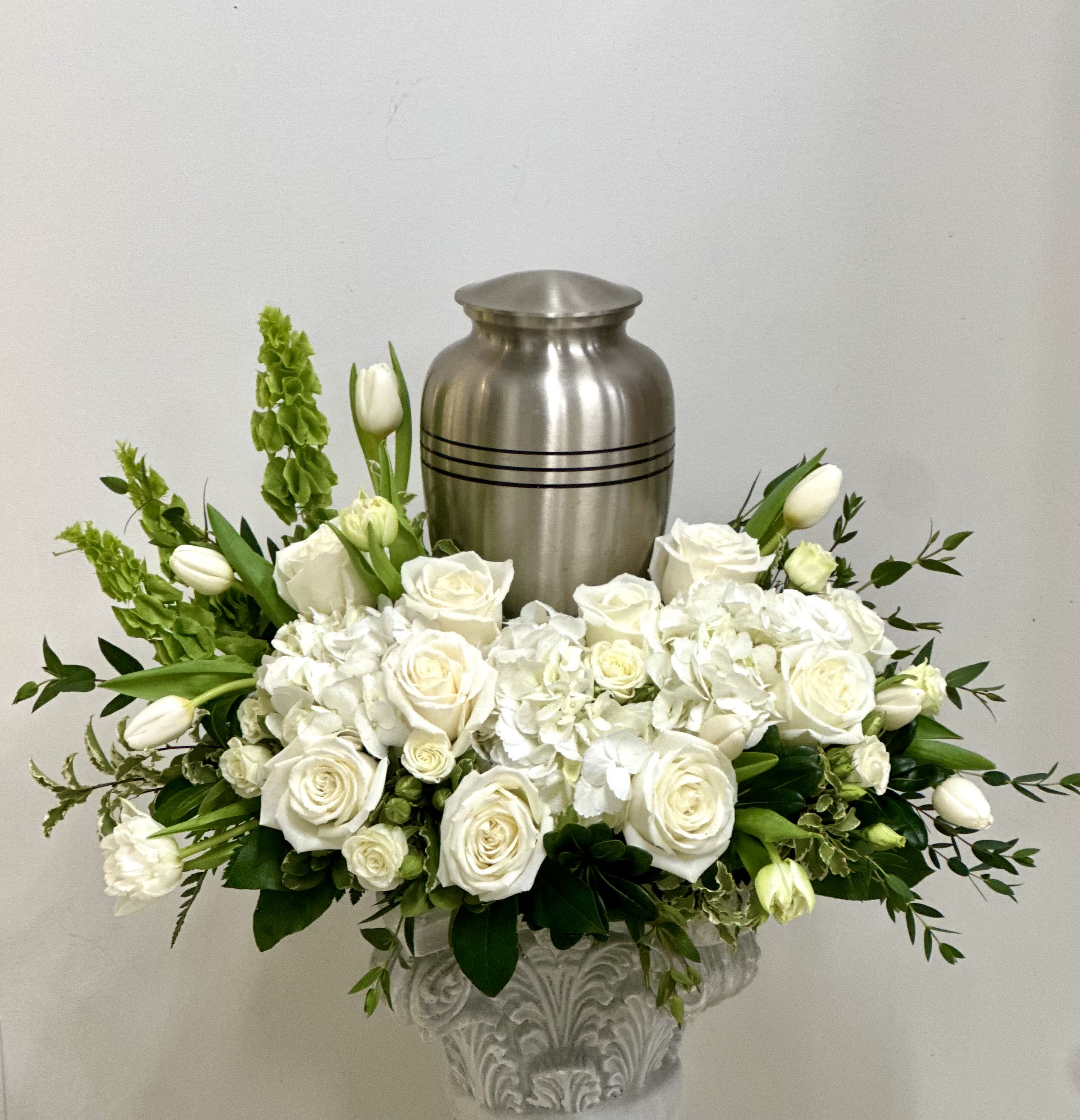 White rose and tulip arrangement in a decorative urn with a silver urn behind it