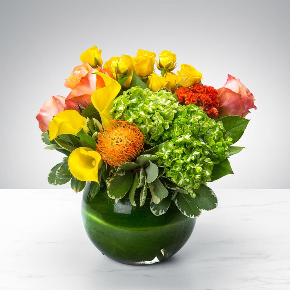 Bouquet of yellow roses, calla lilies, and green hydrangeas in a green glass vase