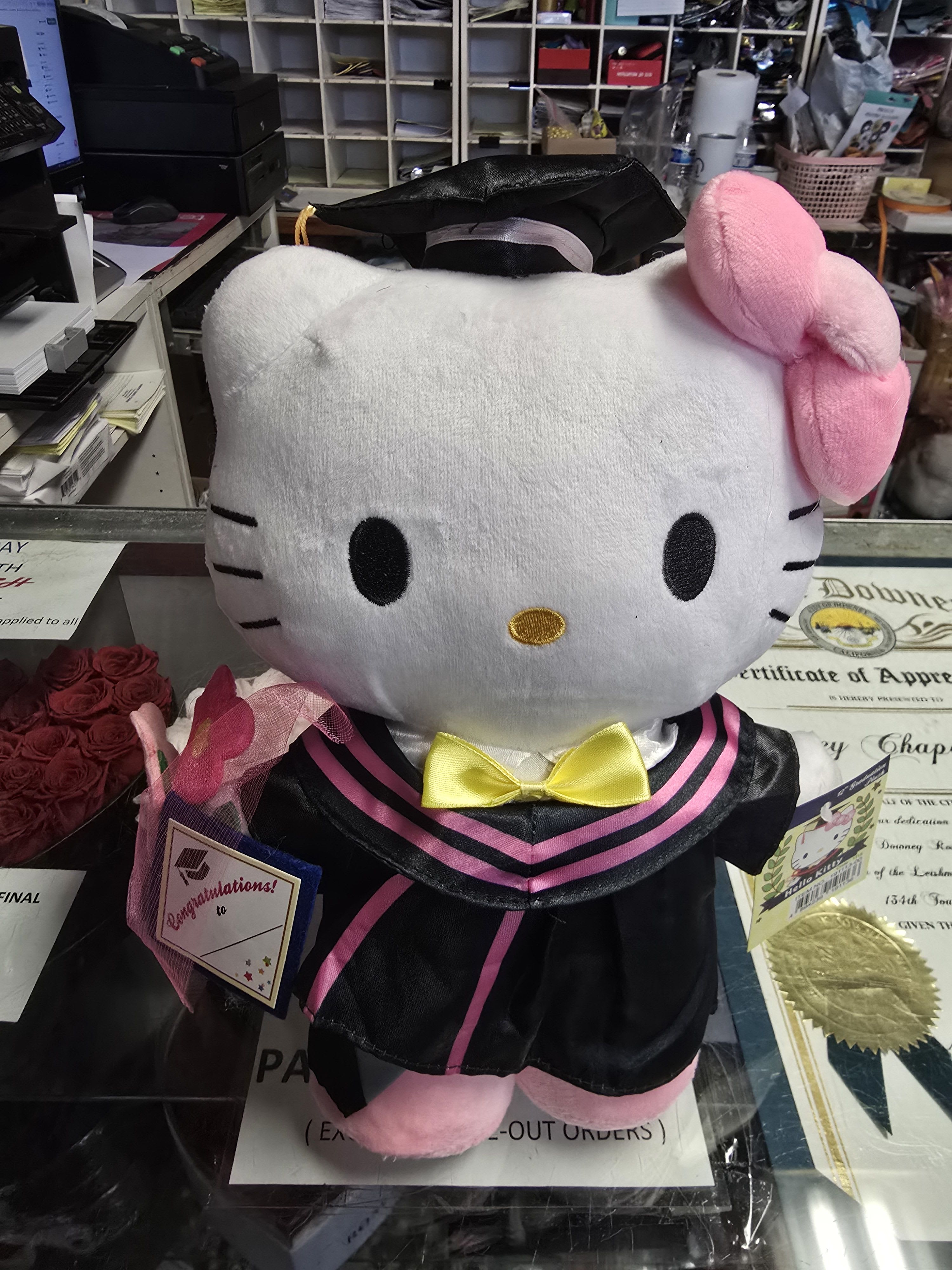 Hello Kitty plush in a graduation outfit with a small rose bouquet