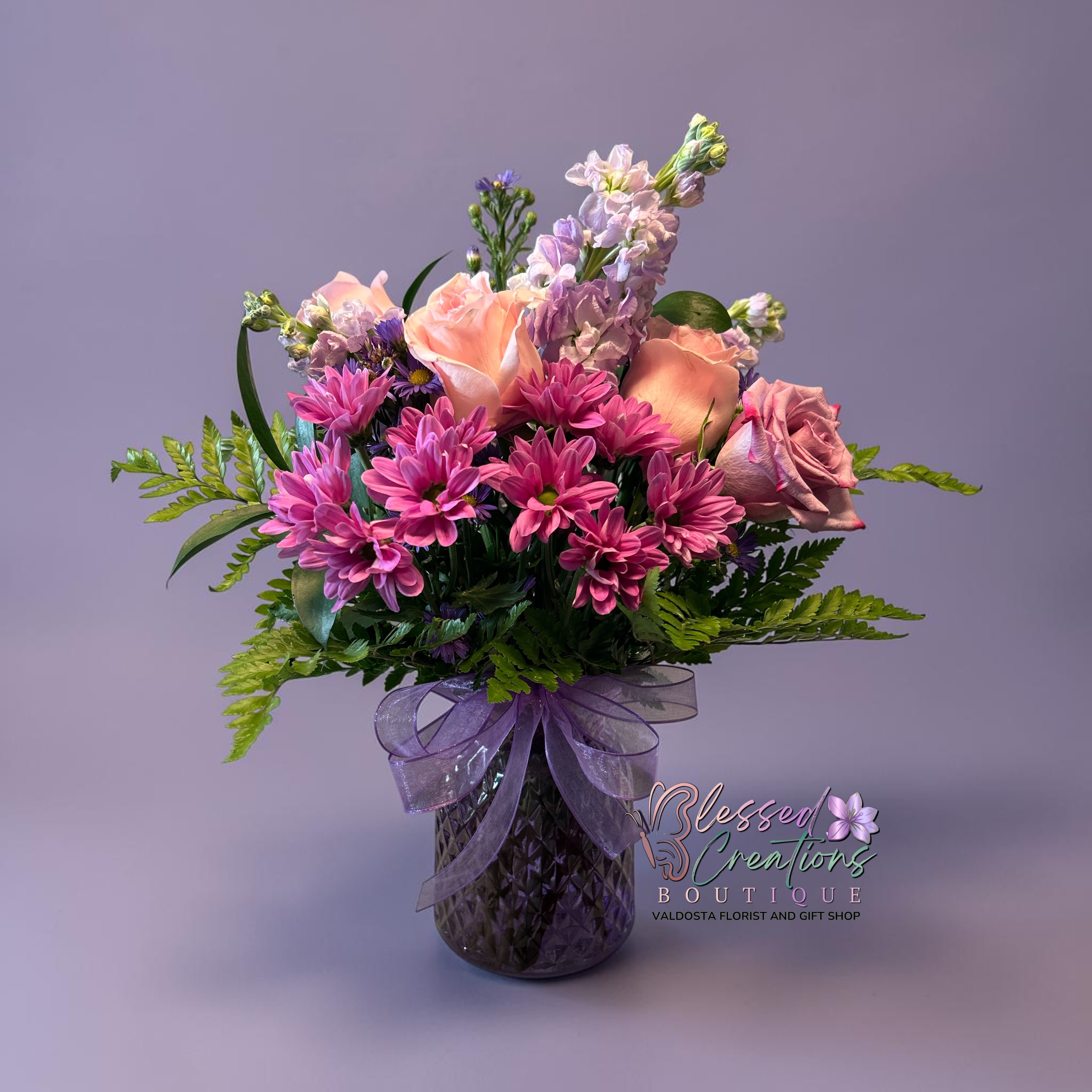 Lavender Blooms  - Elegant fresh flower arrangement with pink roses, lavender roses, lavender stock, purple daisies, and lush greenery in a lavender keepsake vase. 