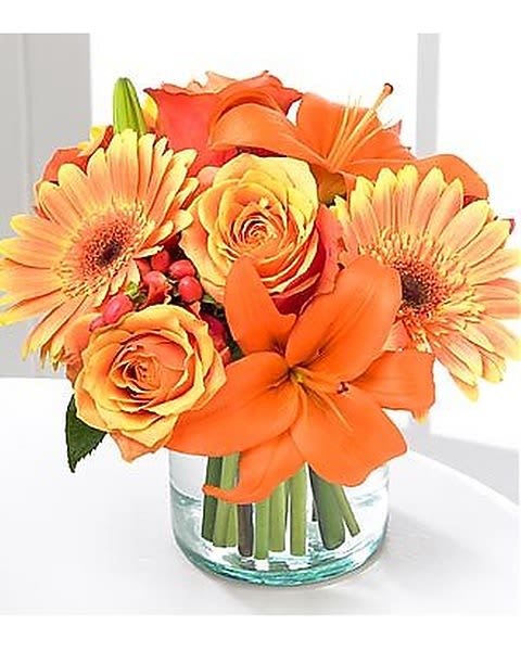 Simply Bewitching - This Bewitching bouquet features orange bi-color roses, orange Gerbera daisies, and orange Asiatic lilies with a touch of red hypericum berries. All are arranged in a flared glass vase, with colors mindful of a beautiful sunset. 