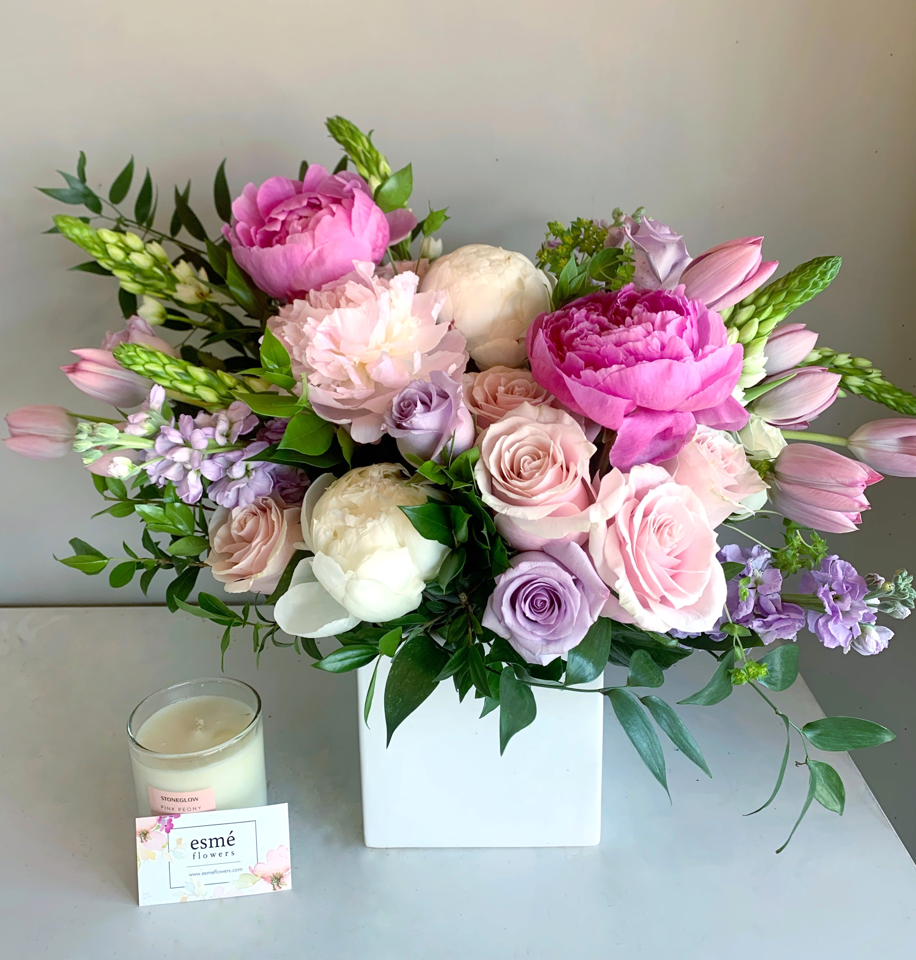 Peony Promise - An assortment of Dutch peonies with ocean song and pink mondial roses, Dutch tulips, in a pristine white ceramic vase. A favorite for Mother's Day! Available for delivery starting Mother's Day Week 5/4.