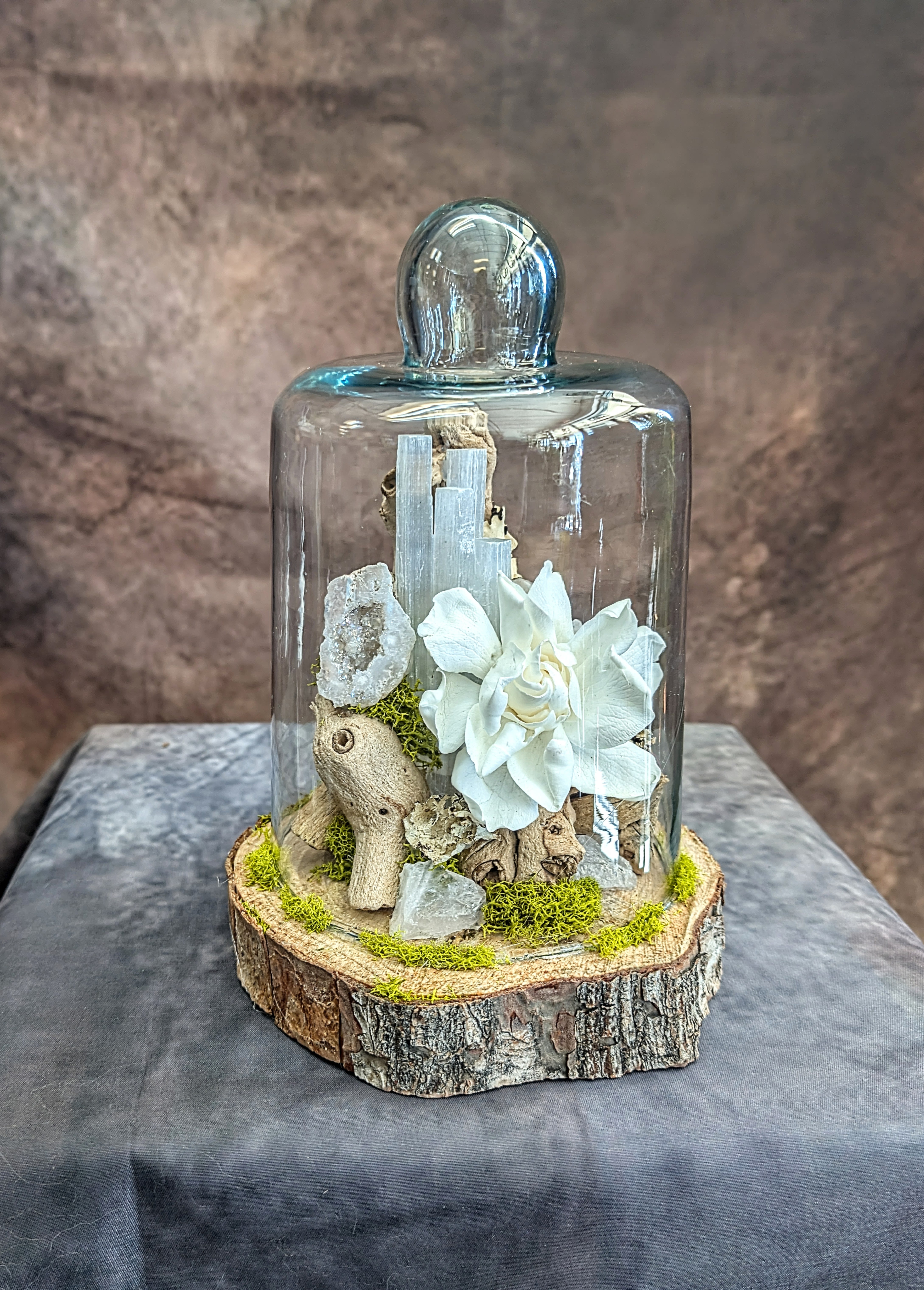 Alba- A Preserved Gardenia Arrangement - Alba is a serene expression of natural elegance, thoughtfully handcrafted at Windmill Floral Expressions in Las Vegas. This preserved gardenia—soft, luminous, and timeless—rests within a glass cloche, surrounded by sculptural selenite, raw quartz, natural wood elements, and touches of vibrant moss. The composition feels both grounded and ethereal, blending organic textures with a quiet, refined beauty.  Each piece is designed as a lasting botanical keepsake, perfect for home décor, meaningful gifting, or adding a subtle sense of calm and luxury to any space. The preserved gardenia maintains its delicate form without the need for water, offering enduring beauty with a modern, nature-inspired aesthetic.  Custom-designed in Las Vegas, Alba is a one-of-a-kind creation. We offer same-day delivery throughout Las Vegas and Henderson, with each design made fresh to order to reflect our commitment to quality, artistry, and individuality.