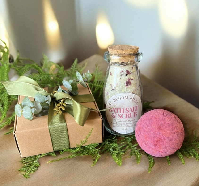 Gift box with ribbon, bath salt jar, and pink bath bomb on greenery