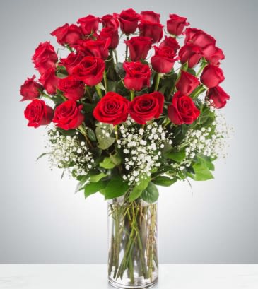 Tall arrangement of red roses with white filler flowers in a clear glass vase