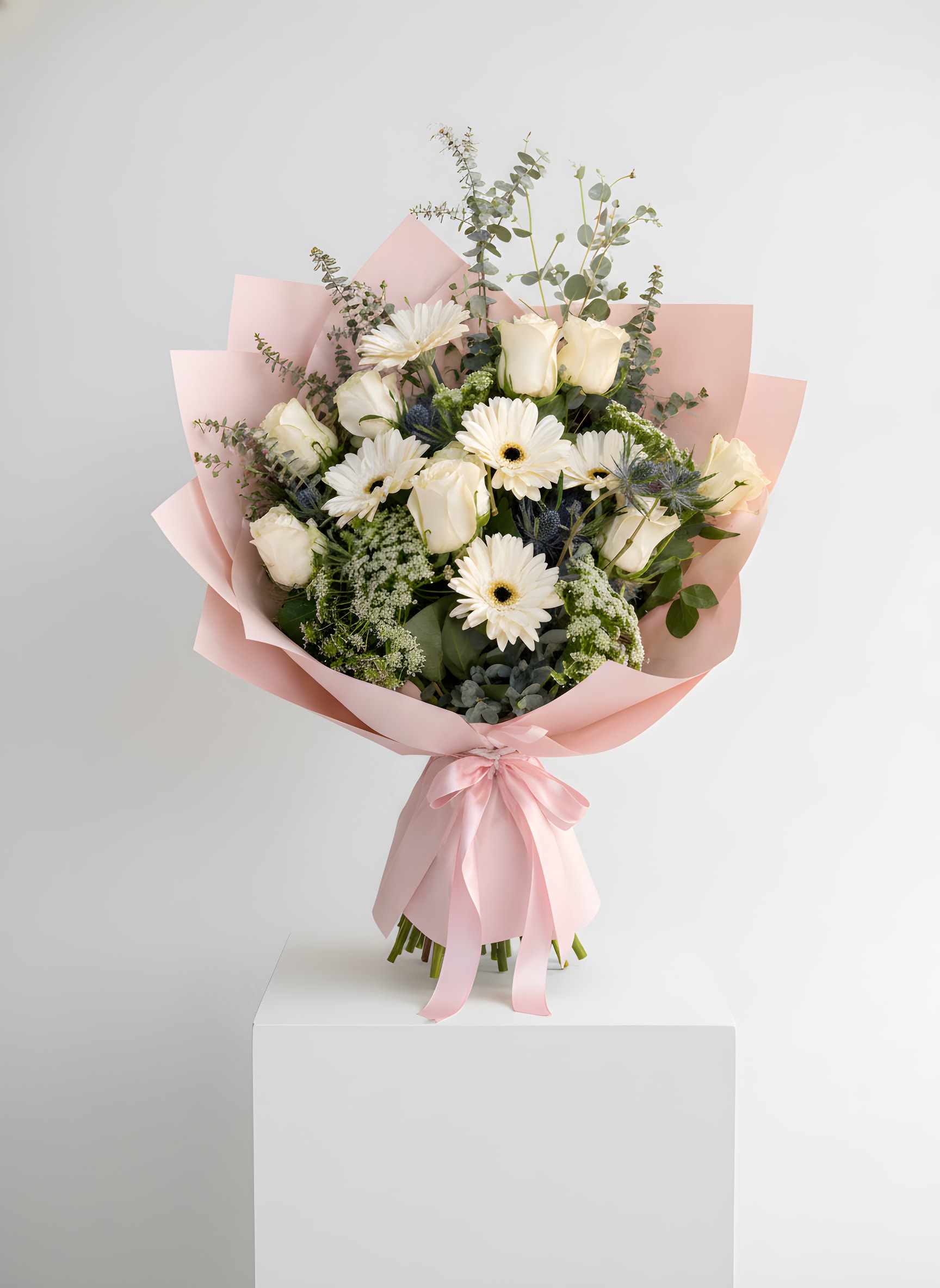 Blush Ivory Bouquet - Elegant, fresh, and softly refined, this bouquet features a delicate blend of ivory roses and creamy white gerbera daisies, accented with airy fillers and cool-toned eucalyptus. The mix of textures creates a natural, garden-inspired look that feels both modern and timeless.