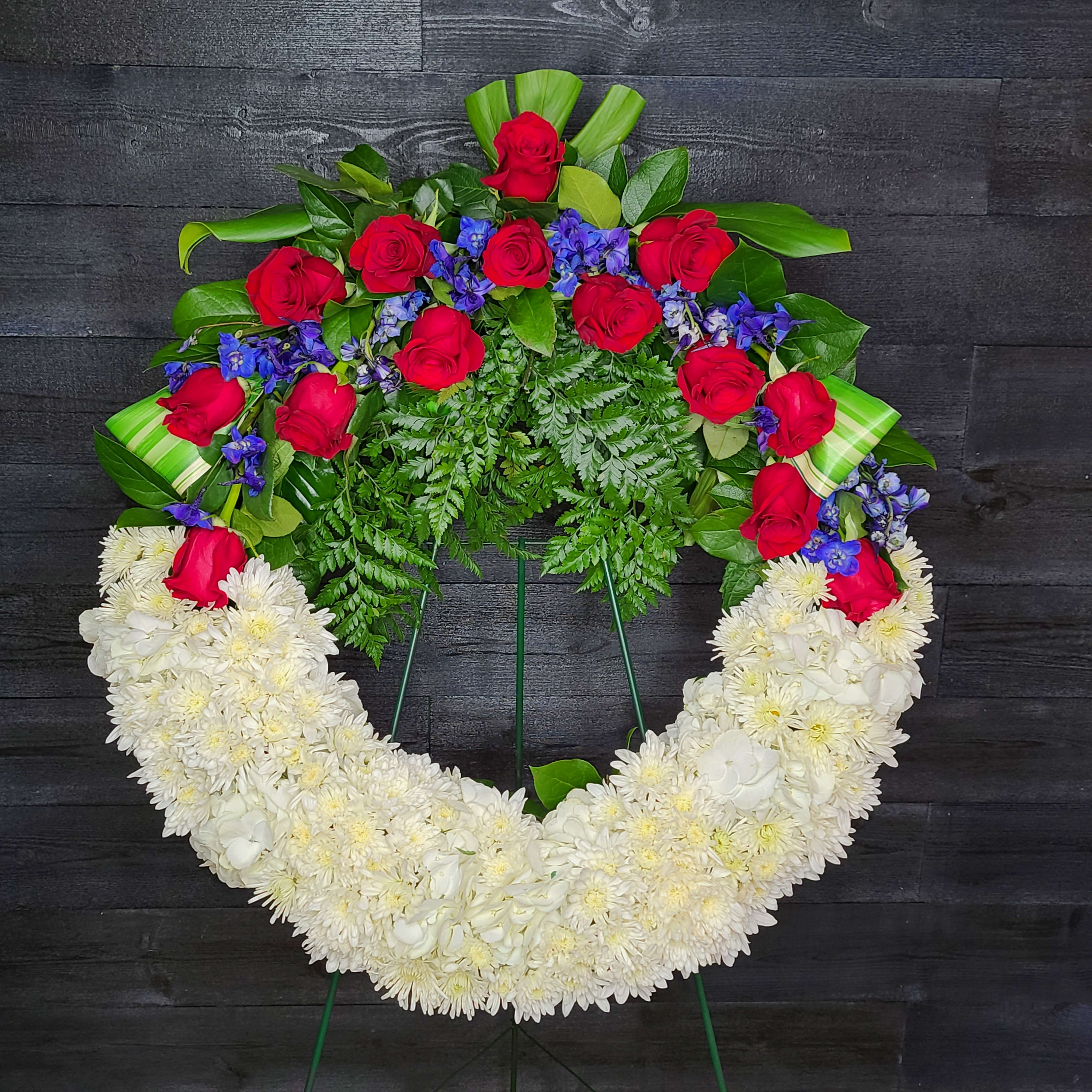 Heart-shaped floral wreath with red roses, blue flowers, and white chrysanthemums