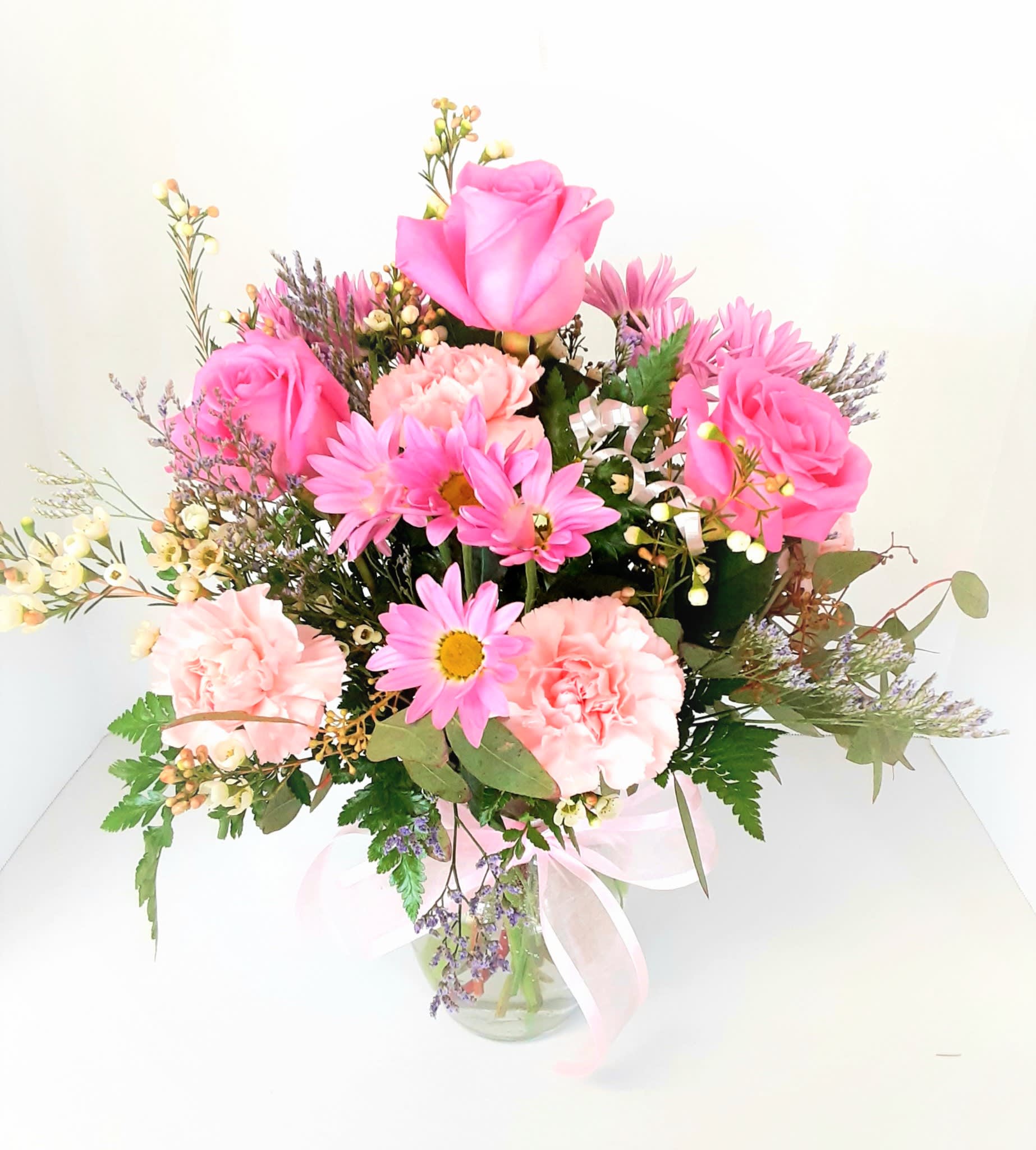 Pink roses and daisies in a clear glass vase with a ribbon