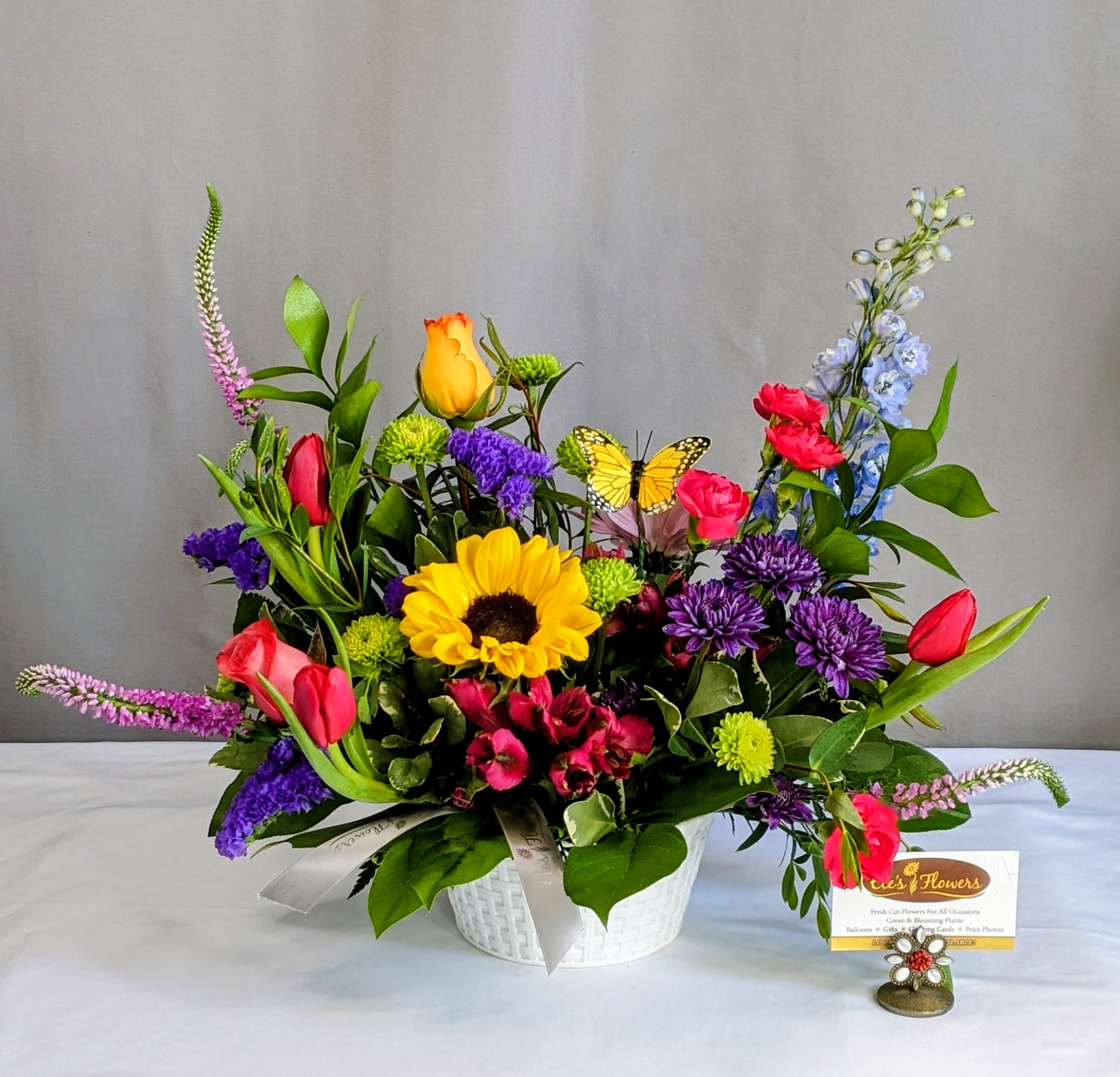Colorful mixed flower arrangement in a white basket with a butterfly pick