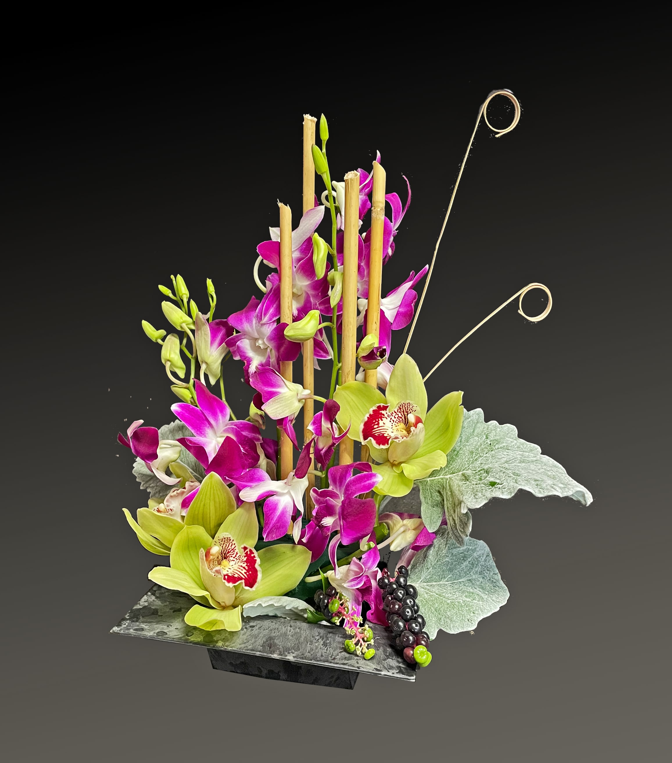 Tall orchid arrangement in a dark rectangular vase with decorative bamboo loops