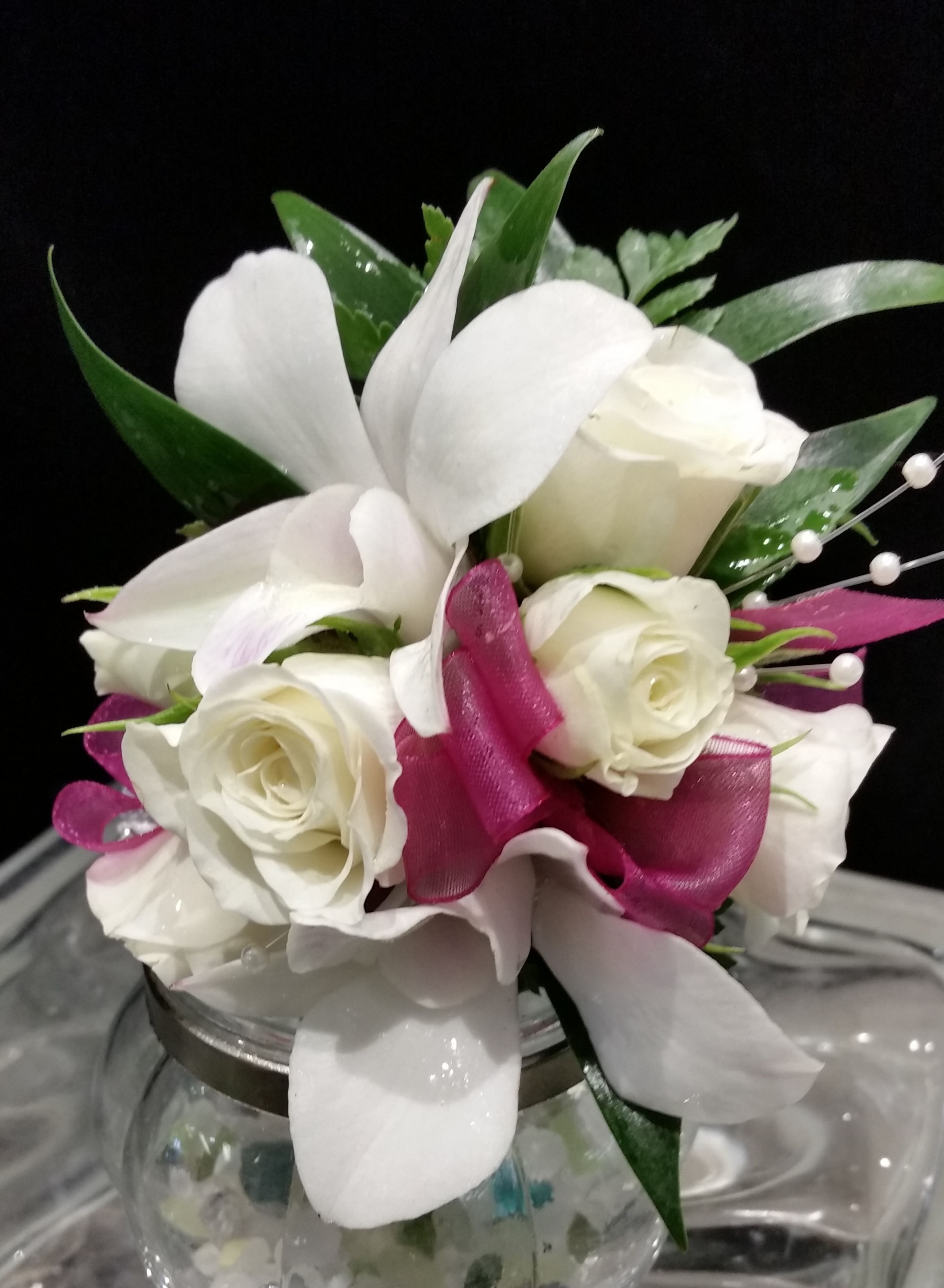 White roses and calla lilies arranged in a glass vase with magenta ribbon accents.