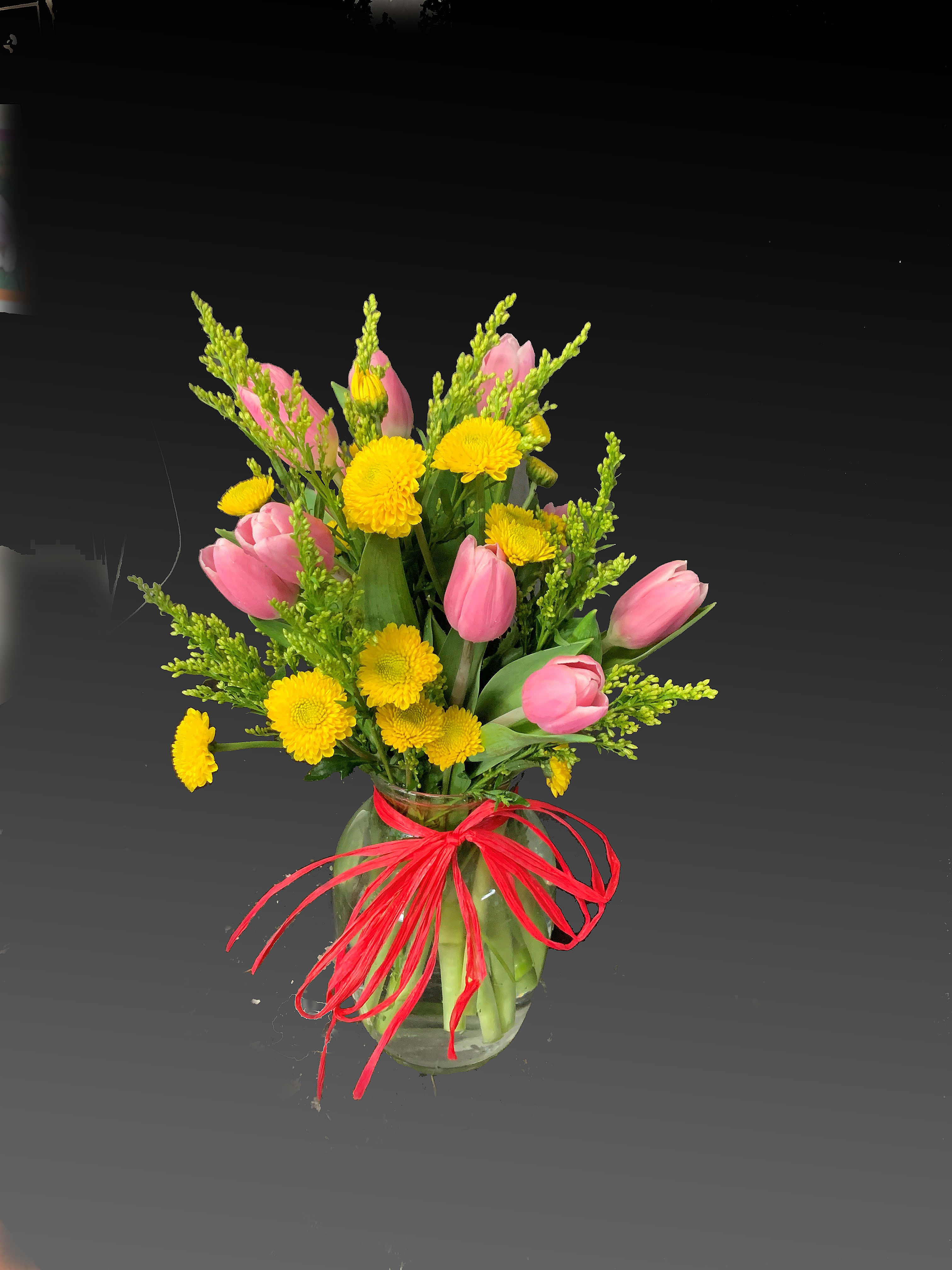 Pink tulips and yellow chrysanthemums in a glass vase with a red ribbon