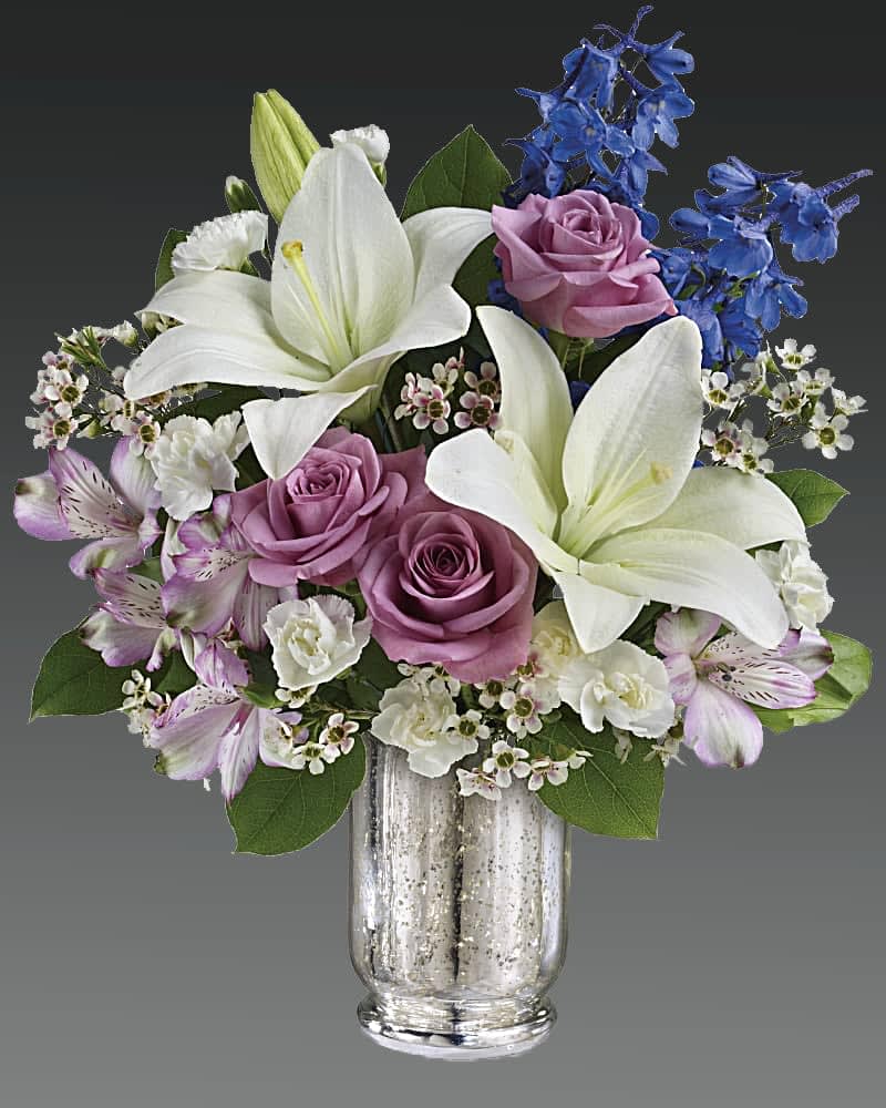White lilies and lavender roses in a glass vase with blue flowers