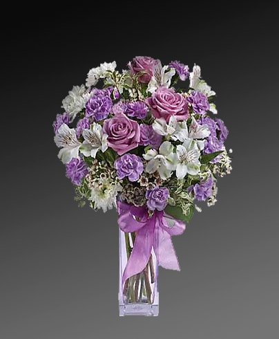 Purple and white bouquet in a clear glass vase with a ribbon