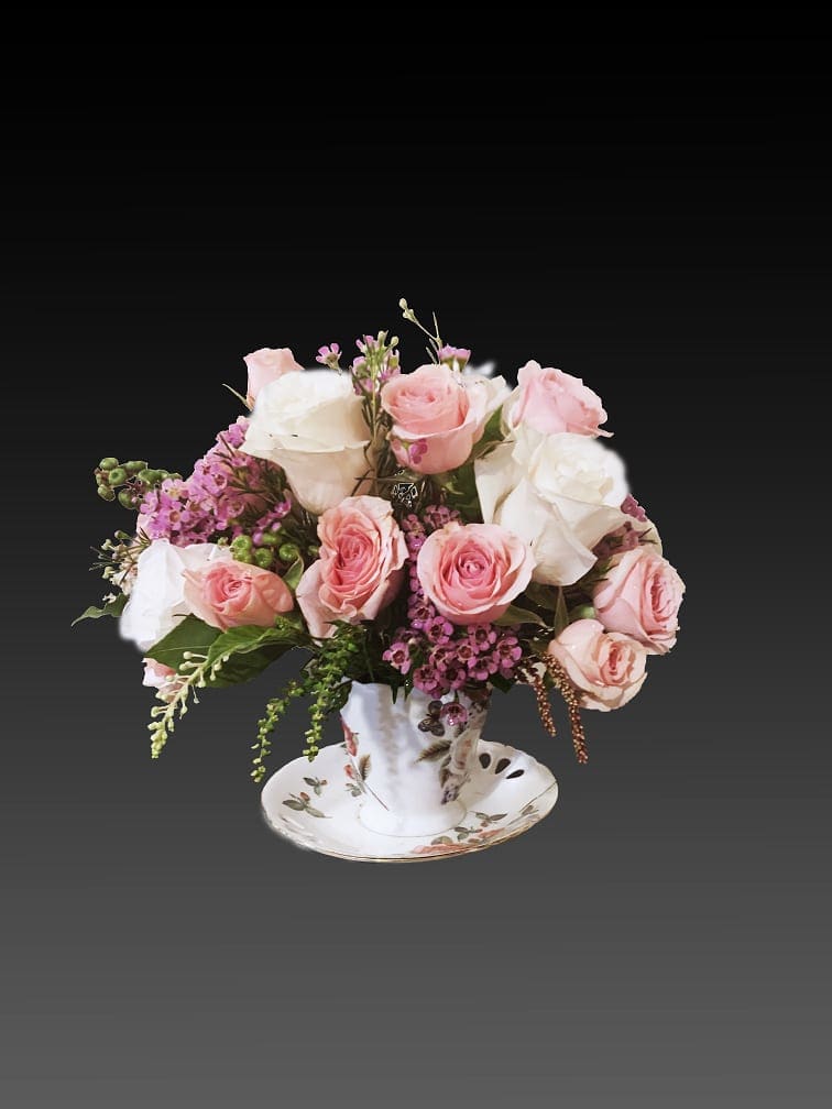 Pink and white roses arranged in a teacup on a saucer