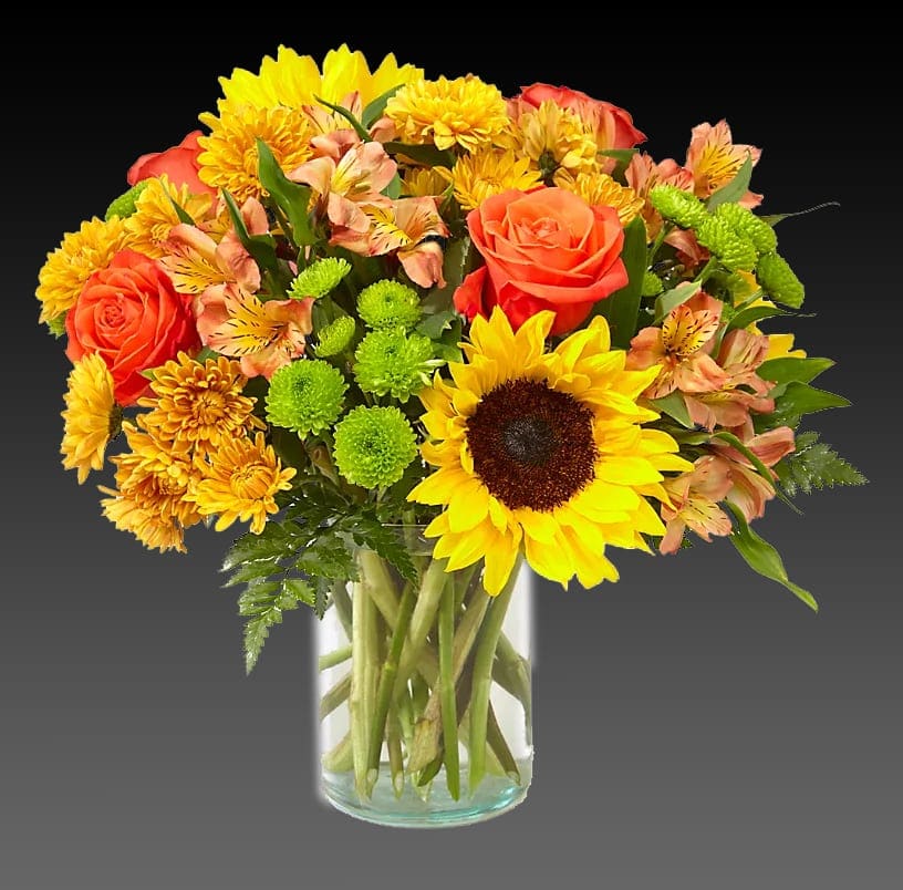 Bouquet of sunflowers, orange roses, and yellow mums in a glass vase