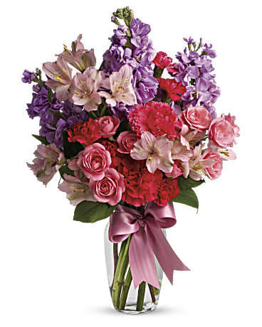 Bouquet of pink and purple flowers in a clear glass vase with a ribbon