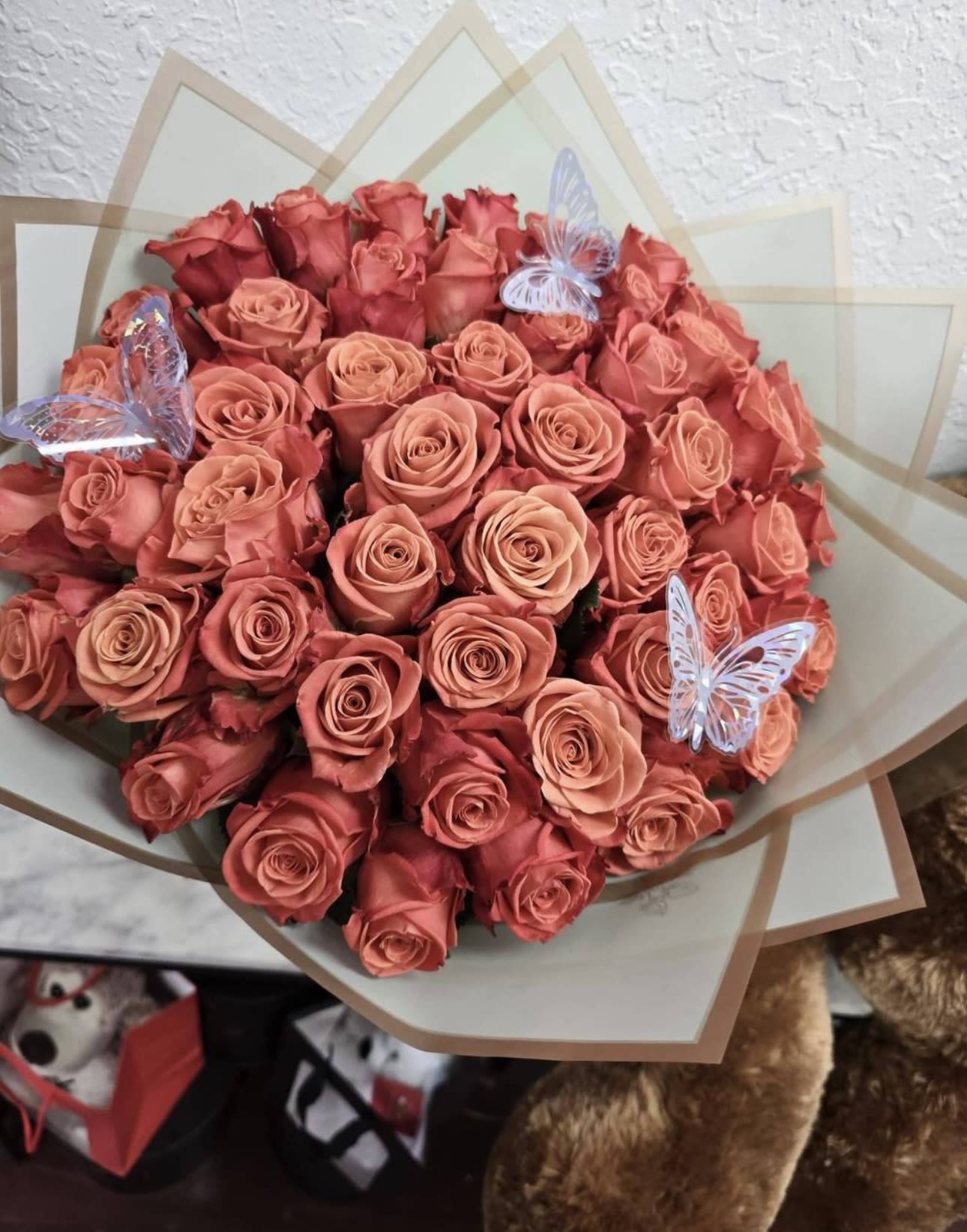 Bouquet of coral and pink roses wrapped in translucent paper with butterfly picks