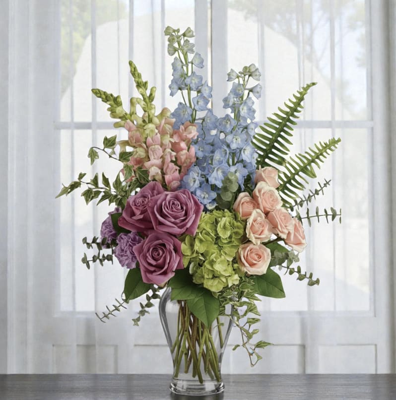 Mixed bouquet of roses, hydrangeas, and blue delphinium in a glass vase