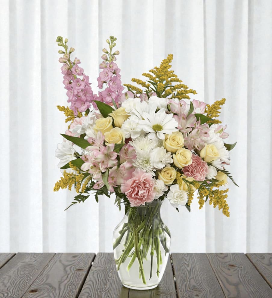 Mixed bouquet of pink, white, and yellow flowers in a clear glass vase