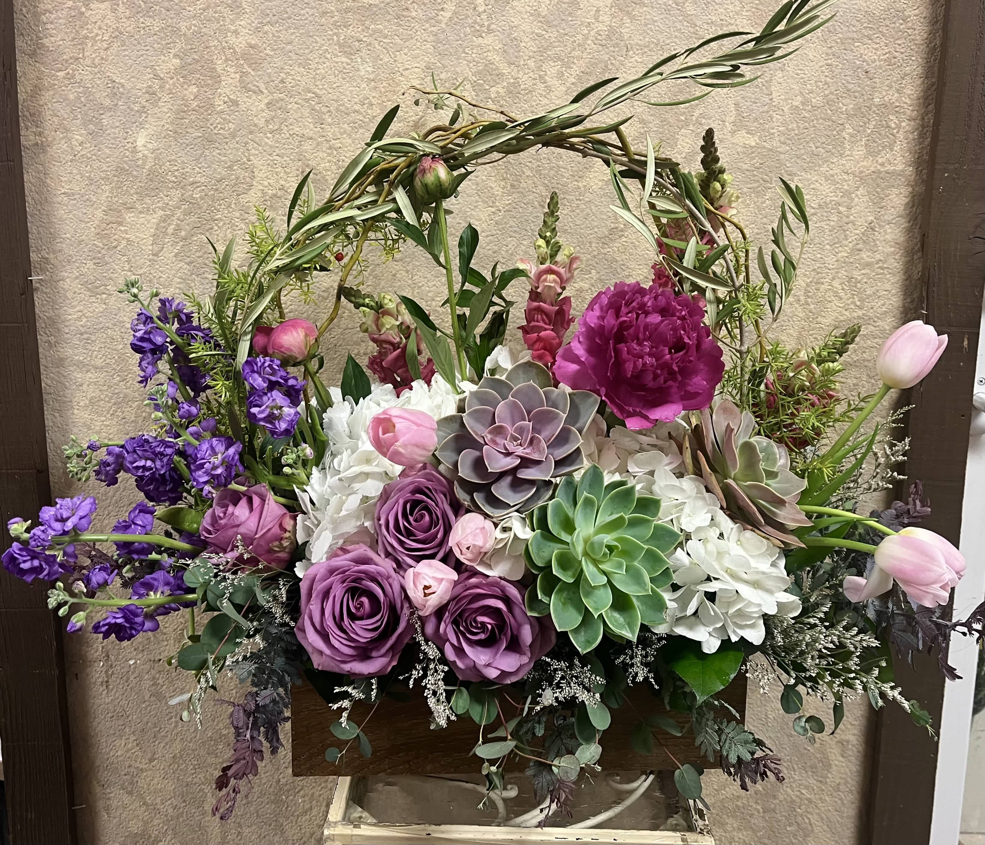 Garden-style arrangement of purple roses, succulents and white hydrangeas in a wooden box.