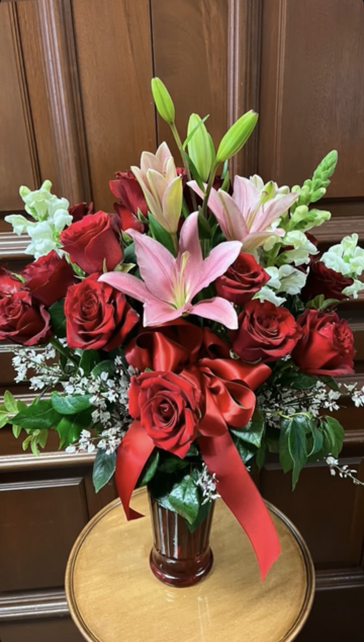 Red roses and pink lilies in a glass vase with a red ribbon