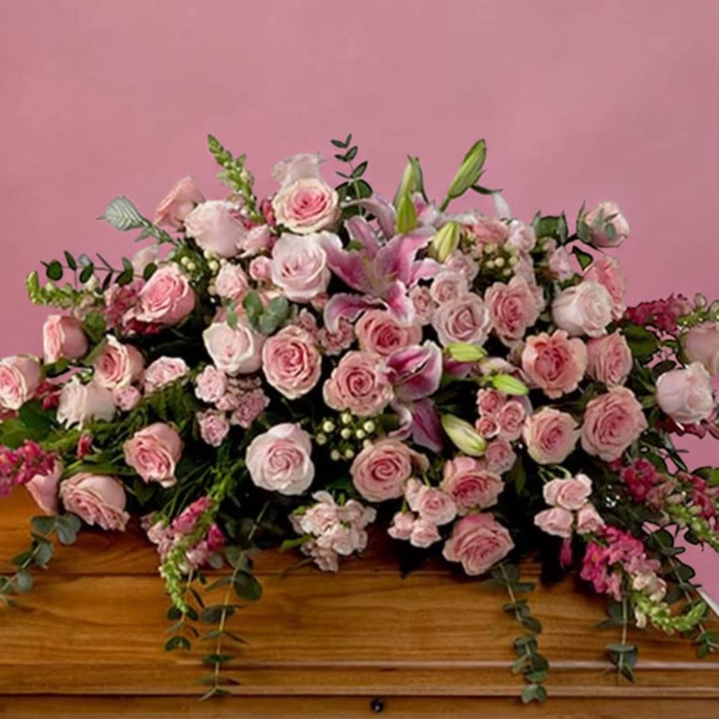 Pink rose and lily casket spray on a wooden casket