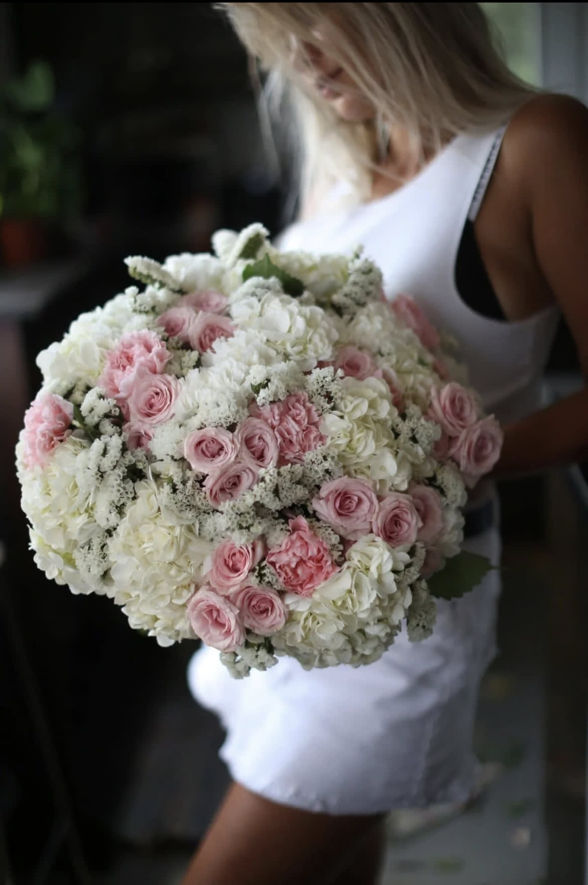 Woman holding a large bouquet of pink and white roses and hydrangeas