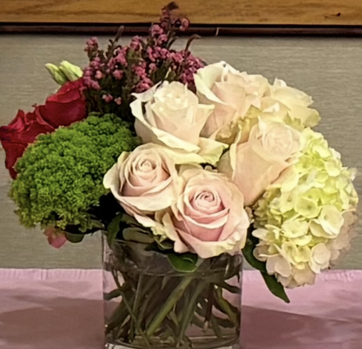 Bouquet of pale roses, hydrangea, and green filler in a glass vase