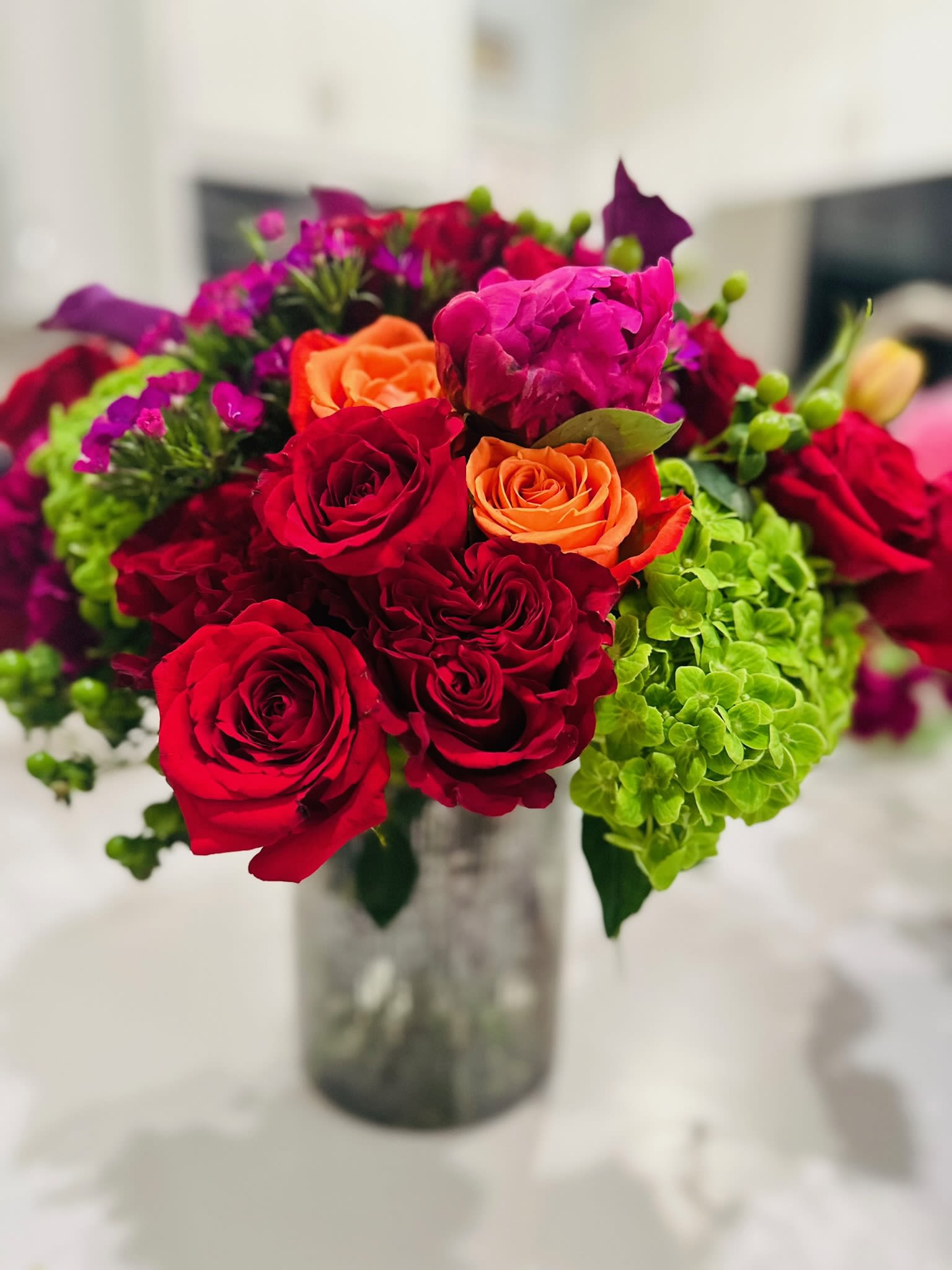 Bouquet of red and orange roses with green hydrangeas in a glass vase