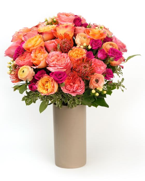 Golden Rose Glow - A lush blend of piink, peach and golden blooms, arranged with fresh greenery for a warm glowing garden feel.