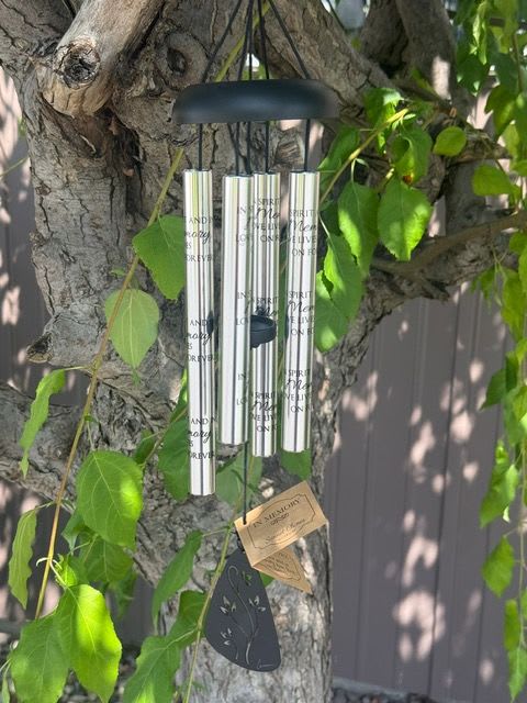 Silver wind chime hanging from a tree branch with green leaves