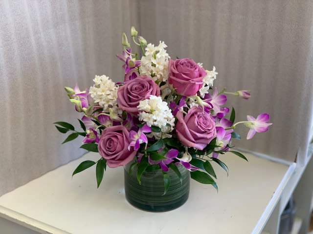 Pink roses and purple orchids arranged in a green glass vase