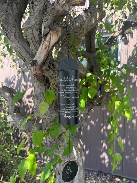 Black memorial wind chime hanging from a tree branch