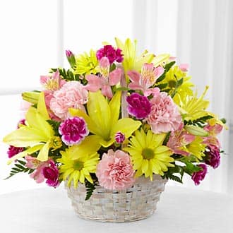 Basket arrangement of yellow lilies, pink alstroemeria, and carnations